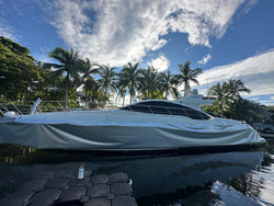 White yacht docked at a marina with palm trees in the background in the process of being wrapped in gray/grey wrap.
