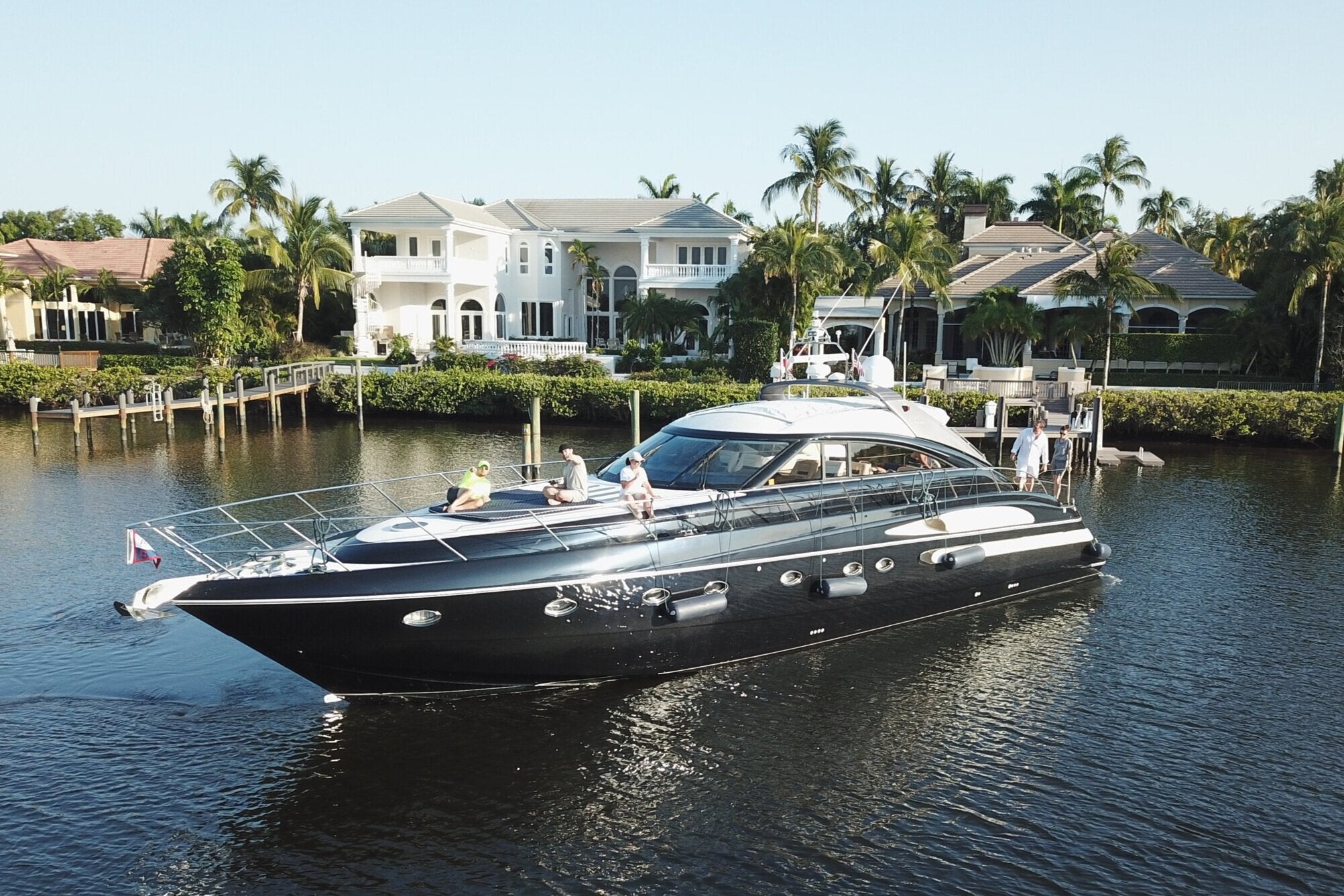 Luxury yacht on a canal with residential houses and palm trees in the background. just finished being wrapped all black with family on oat.